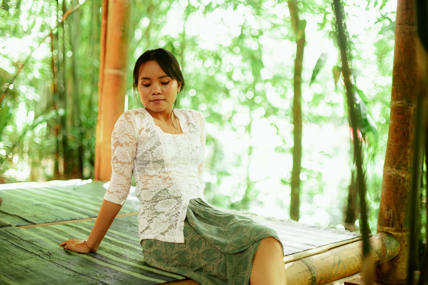 Asian Woman In White Kebaya and Batik Sitting Barefoot In a Shack Lush Greenery Garden